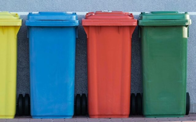 four assorted-color trash bins beside gray wall